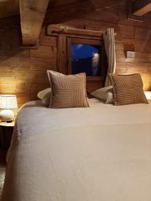 Lit double dressé dans un chalet avec des lampes de chevet allumées dans le fond