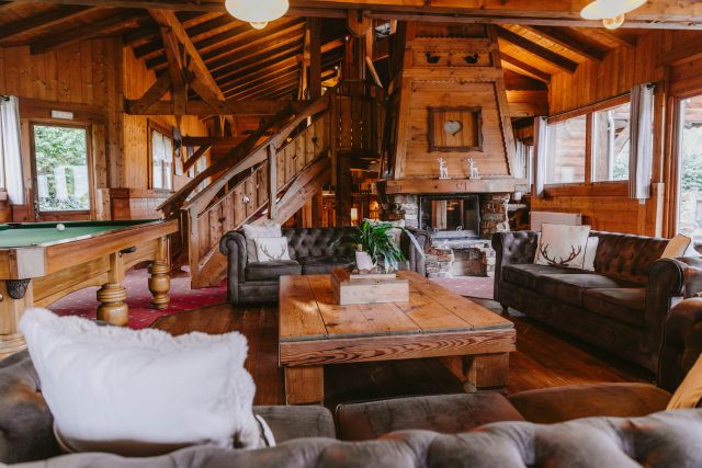 Salon chaleureux dans un chalet en bois avec canapé confortable, télévision et table de billard.