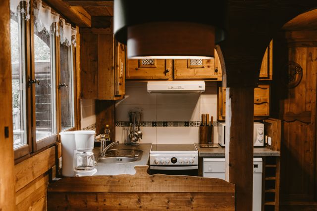 Cuisine en bois dans un chalet, équipée d'une machine à laver, d'une gazinière, d'un évier, d'un micro-onde et d'une fenêtre avec vue sur les montagnes.