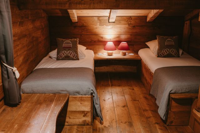 Chambre dans un chalet en bois avec deux lits simples disposés de chaque côté, ambiance chaleureuse et rustique.