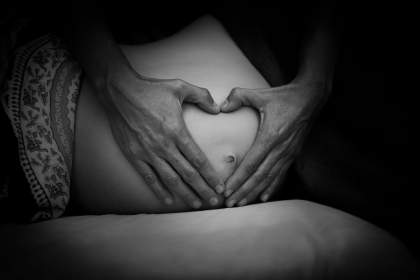 Ventre arrondi d'une femme enceinte avec des mains posées dessus formant un coeur.