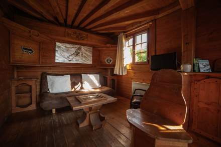 Salon dans un chalet en bois avec canapé, chaise, TV, fenêtre et décoration