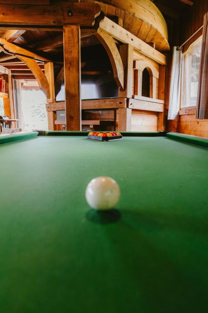 Salon chaleureux de chalet en bois avec billard, canapé confortable et cheminée rustique.