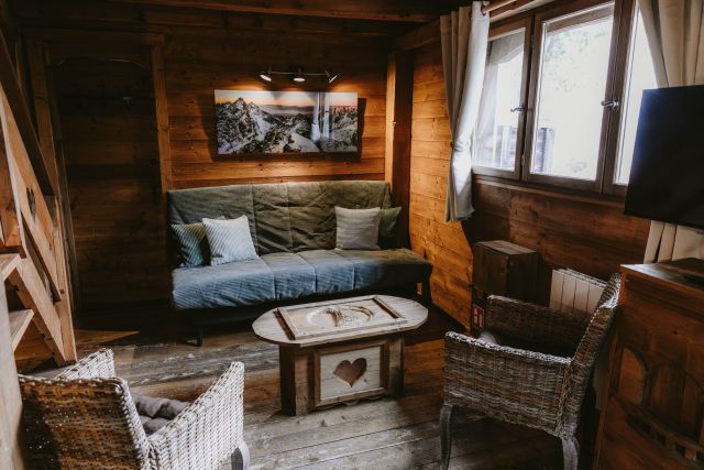 Salon chaleureux dans un chalet en bois, avec canapé confortable et télévision murale.